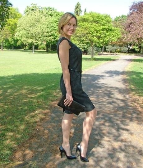 Clothed business woman shows off her sexy legs in high heels in the park