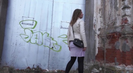 Short taken girl Rita squats for a piss behind a building in the countryside