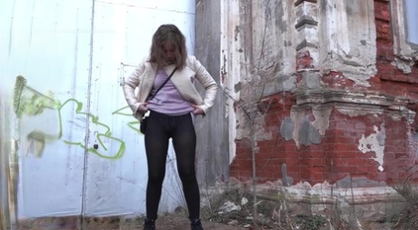 Short taken girl Rita squats for a piss behind a building in the countryside