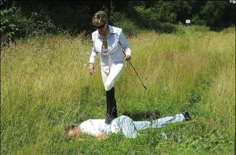 Busty mature femdom in sunglasses humiliates her boy slave outdoors